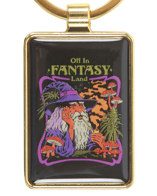 Steven Rhodes Fantasy Land keyring from Rebel Romance. A retro-style enamel design in a gold frame, featuring a wizard in a purple hat smoking a pipe surrounded by red mushrooms and magical plants with the text “Off in Fantasy Land.” A quirky alternative gift for millennials who love gothic, witchy, and whimsical aesthetics.