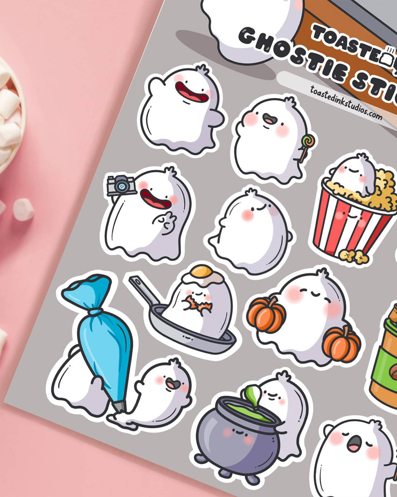 Zoomed-in view of Toastedink ghostie stickers on a grey background with playful designs including a ghost in a frying pan and another casting a spell. A cute stationery essential from Rebel Romance, a UK-based shop for fun and whimsical gifts.