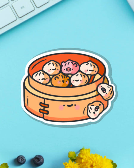 Steamed Buns Vinyl Sticker on a bright blue background. Adorable dim sum characters including tiger, pig and classic dumplings in a cheerful bamboo basket. From Toastedink, stocked by Rebel Romance – a UK small biz embracing playful, foodie vibes and alt style.