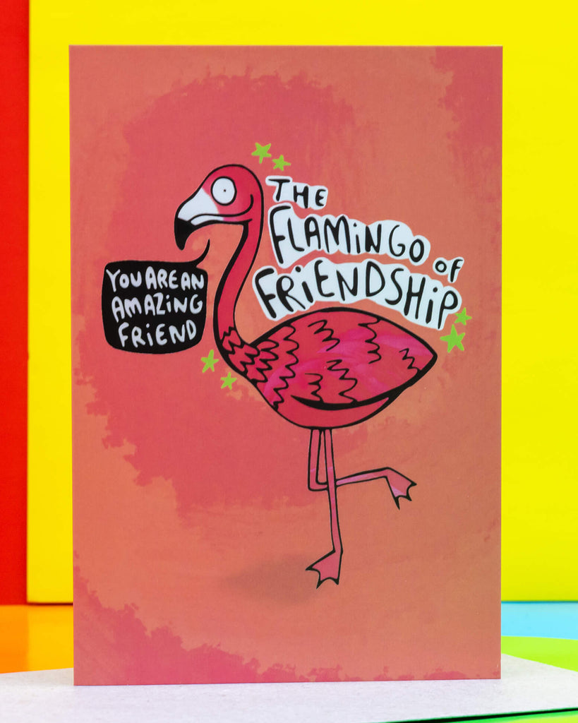 A colourful A6 greetings card by Rebel Romance featuring a pink illustrated flamingo on a coral-pink background. The flamingo is saying "You are an amazing friend" in a speech bubble, with the words "The Flamingo of Friendship" above. Designed by Katie Abey, this quirky card is perfect for sending love to a fabulous friend. Ideal for alternative gift-givers who love fun, bold stationery with personality. Blank inside with envelope included.