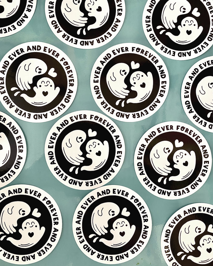 Multiple Forever and Ever Ghostie Stickers stocked at Rebel Romance are displayed on a blue surface. The round black-and-white stickers feature two cute ghosts in love surrounded by the phrase “FOREVER AND EVER AND EVER AND EVER.” Illustrated by Yasmin Cousins and ideal for adding charm to notebooks, laptops, or gifts.