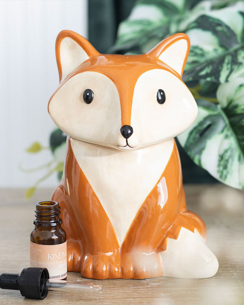 Lifestyle image of the Rebel Romance fox oil burner and wax warmer on a wooden surface, next to a bottle of essential oil. The fox has a cute face and woodland colours, ideal for cosy home décor lovers.