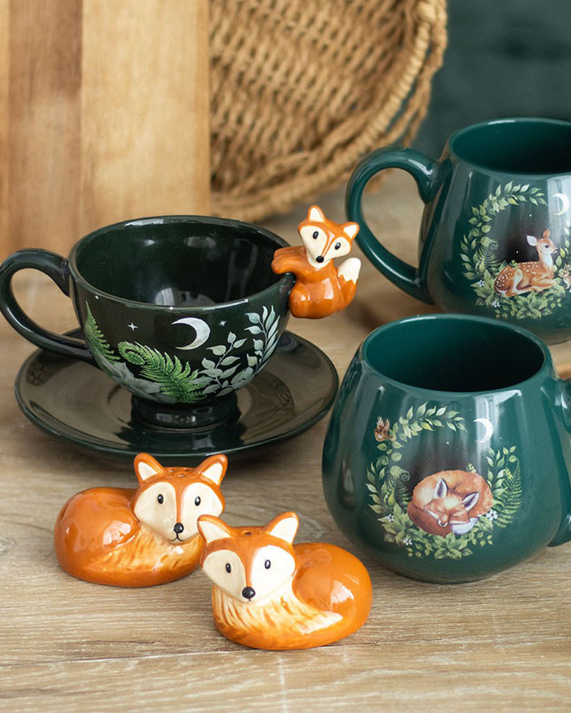 Styled image of woodland-themed ceramic kitchenware including two fox-shaped salt and pepper shakers, a mug with a fox design, and a cup with a fox perched on the rim.