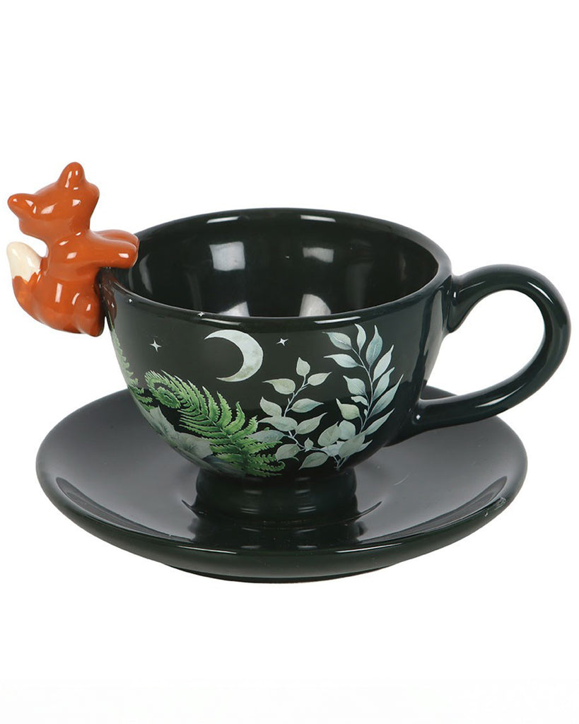 Close-up of the Rebel Romance green forest ceramic teacup with saucer, featuring a 3D orange fox perched on the rim and leafy moonlit woodland design. A magical teacup for cosy tea moments.
