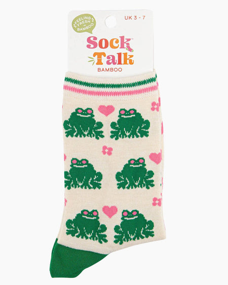 A pair of cream-coloured bamboo socks featuring a fun green frog pattern with pink love hearts and flowers. The socks have a striped green and pink cuff, green heels, and pink soles with ‘Sock Talk’ branding