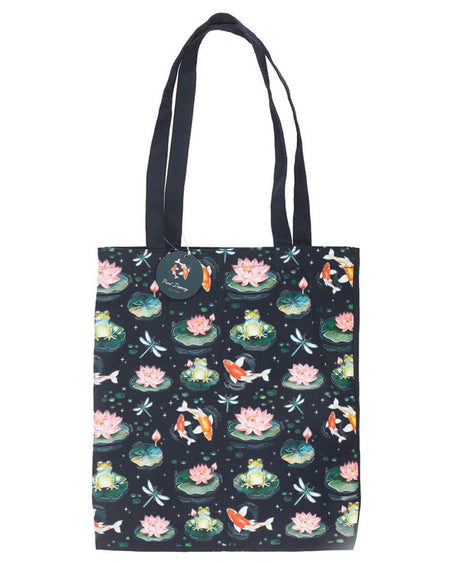 Full view of the navy blue tote bag showing the detailed pond-inspired pattern with frogs, koi fish, lily pads, and dragonflies. The bag hangs against a plain white background with a circular brand tag attached to the handle.
