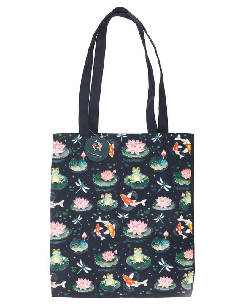 Full view of the navy blue tote bag showing the detailed pond-inspired pattern with frogs, koi fish, lily pads, and dragonflies. The bag hangs against a plain white background with a circular brand tag attached to the handle.
