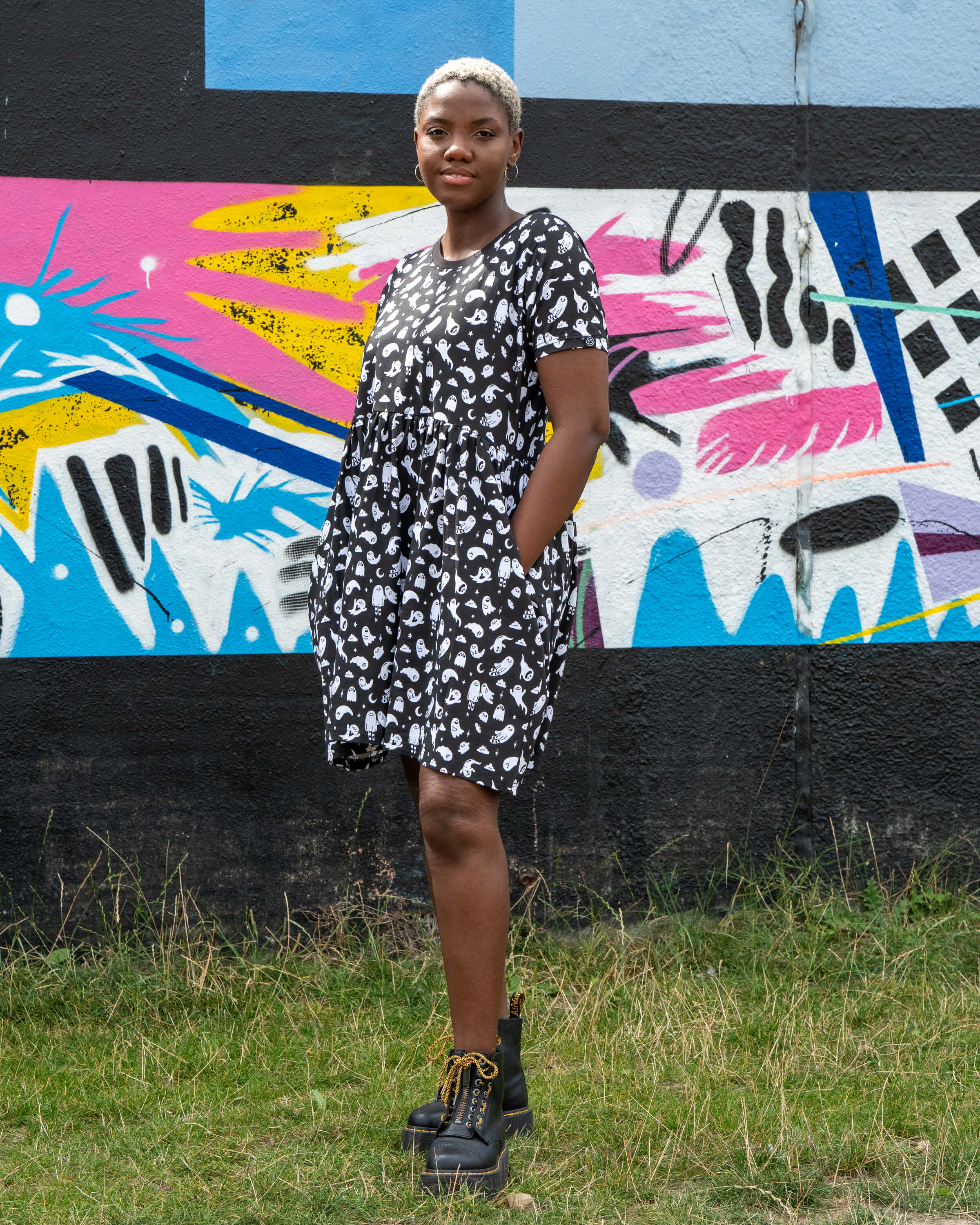 Chish models a stretch cotton smock dress featuring an all-over white ghost print. This alternative casual dress has short sleeves, side pockets, and a relaxed fit, ideal for everyday gothic and quirky style.