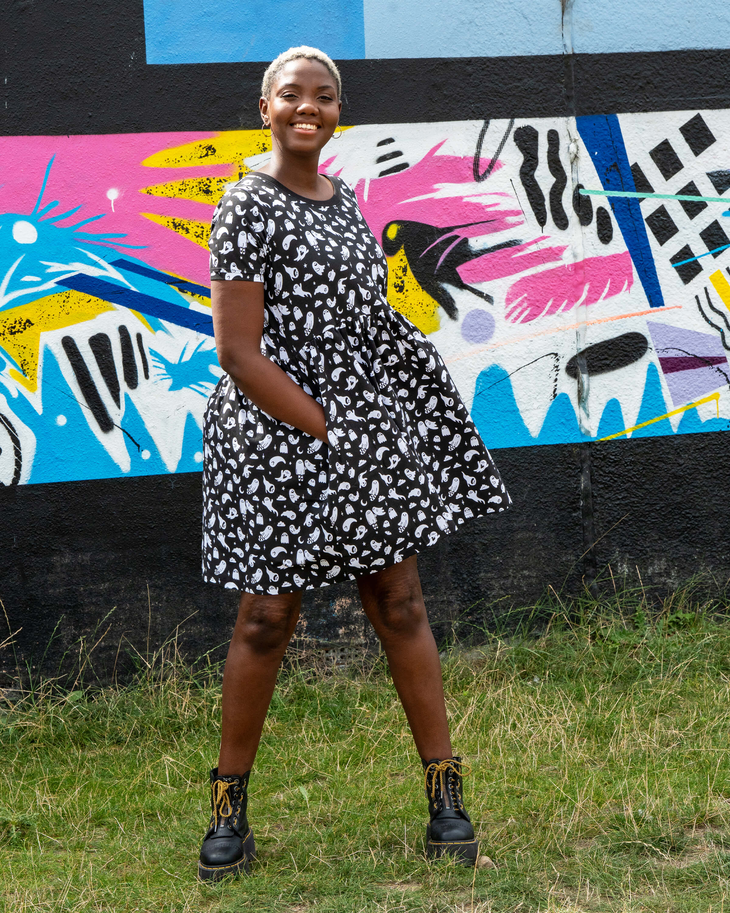 Chish models a stretch cotton smock dress featuring an all-over white ghost print. This alternative casual dress has short sleeves, side pockets, and a relaxed fit, ideal for everyday gothic and quirky style.