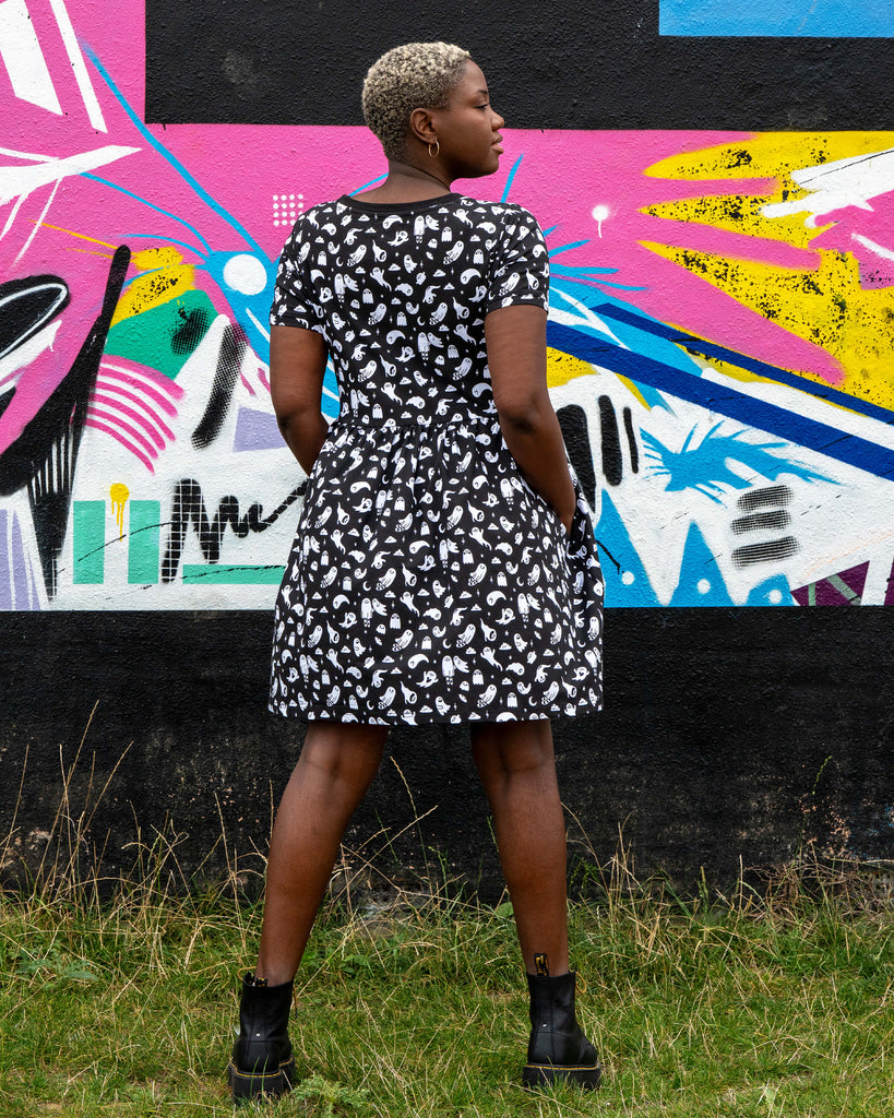 Back view of the Rebel Romance Ghosties Smock Dress worn by Chish. The black stretch cotton fabric is covered in a cute white ghost pattern, showing the relaxed fit and short sleeves.
