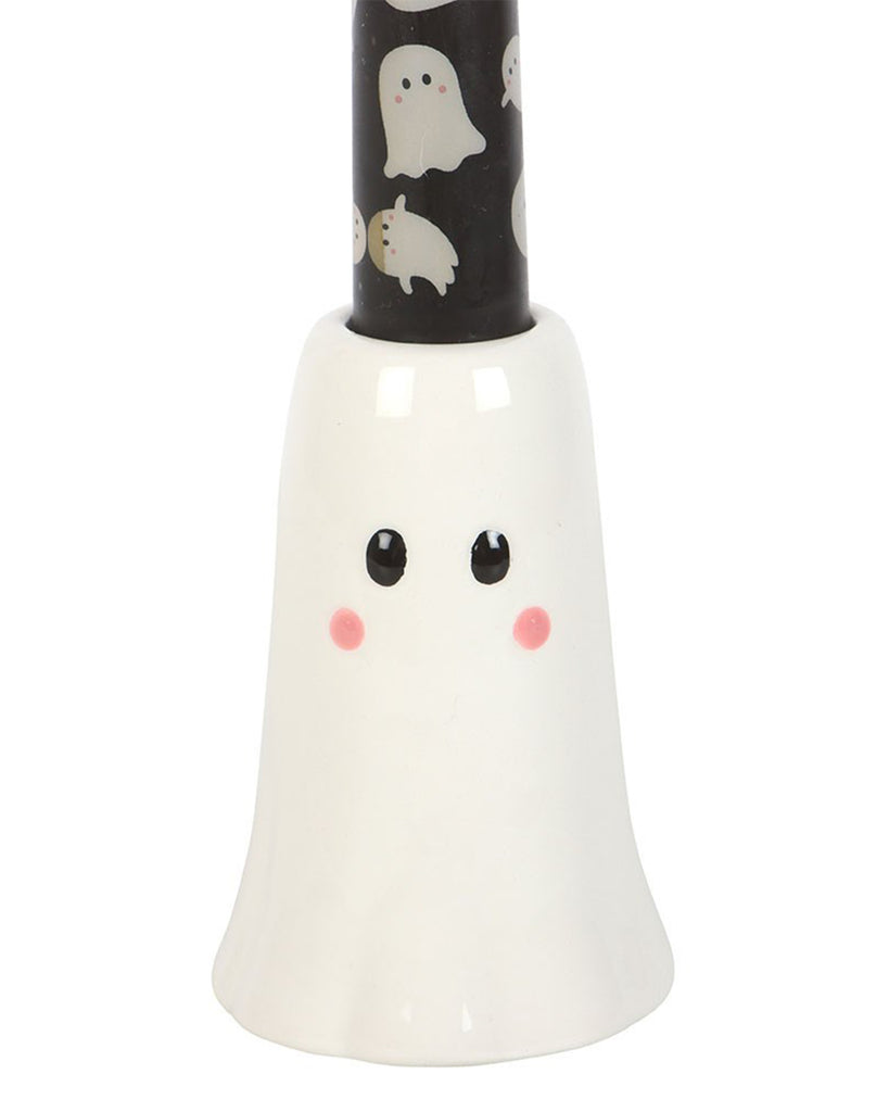 Close-up of the ceramic ghost candle holder base from Rebel Romance, with glossy white ceramic, painted black eyes, and pink cheeks. The black taper candle with white ghost print is securely held in place.