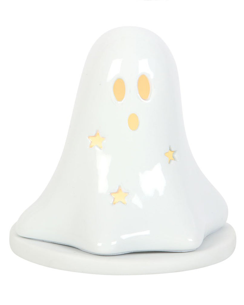 The ceramic ghost tealight holder glowing warmly from within, with light beaming through star and face cut-outs. A whimsical Halloween-themed ornament from Rebel Romance UK, ideal for cosy nights or witchy home décor enthusiasts.