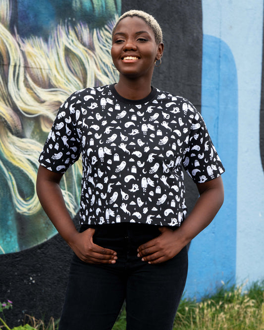Chish wearing a black t-shirt with white ghosties illustrated by Yasmin Cousins against a colourful mural background