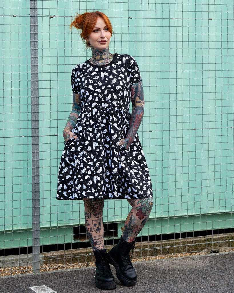 Erin models a stretch cotton smock dress featuring an all-over white ghost print. This alternative casual dress has short sleeves, side pockets, and a relaxed fit, ideal for everyday gothic and quirky style.