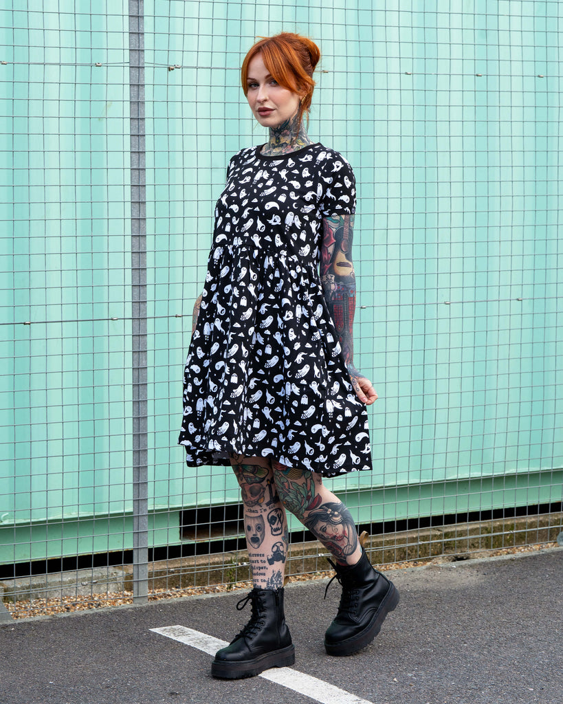 Erin models the Rebel Romance Ghosties Smock Dress. The black cotton dress has a playful white ghost pattern, smock fit, and short sleeves, shown styled with black boots.
