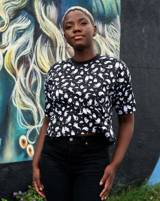 Chish wearing a black t-shirt with white ghosties illustrated by Yasmin Cousins against a colourful mural background