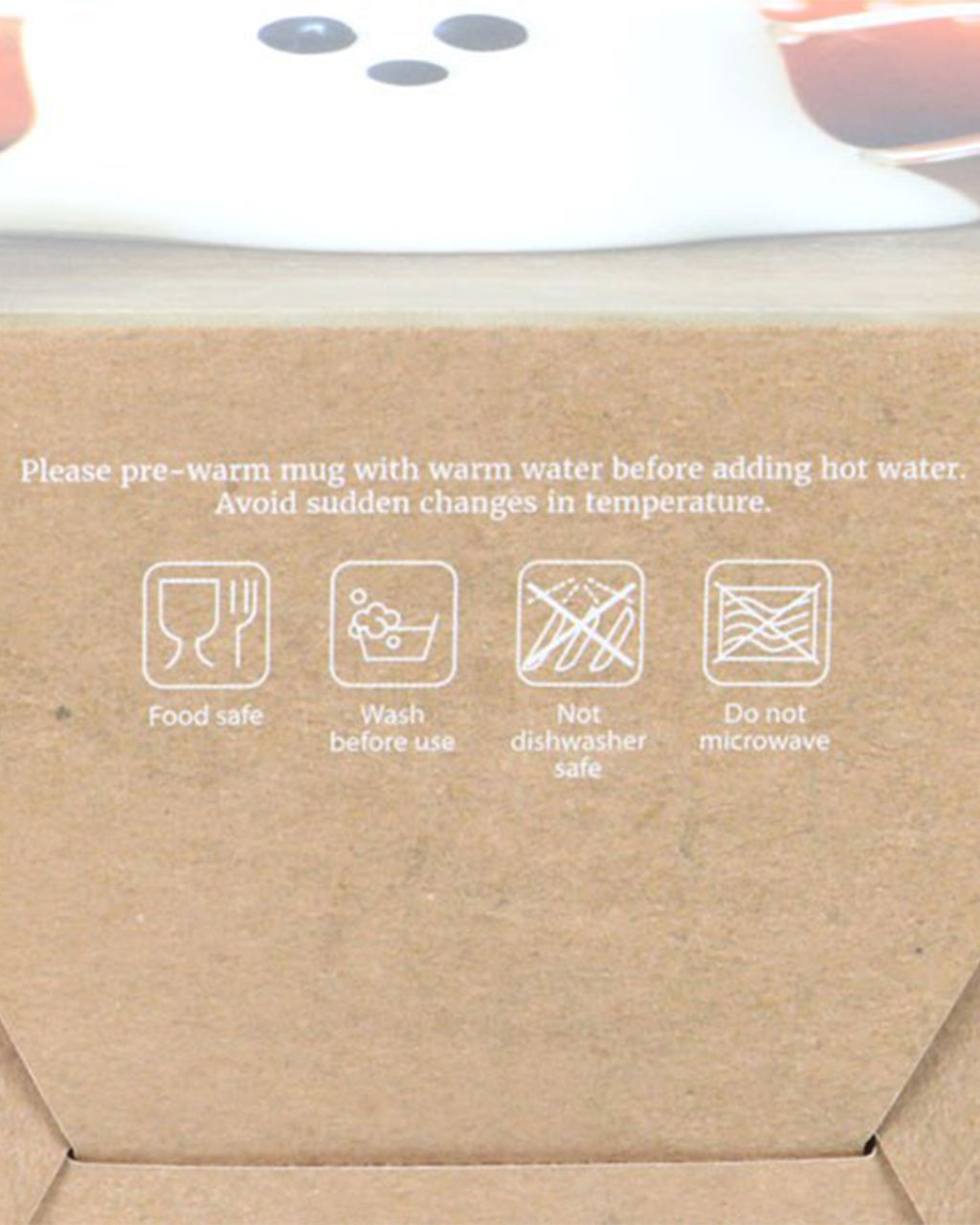 A close-up of the inside of the Ghost Shaped Glass Mug’s packaging from Rebel Romance, displaying care instructions. The box advises pre-warming before adding hot liquids and warns against dishwasher and microwave use. White icons and text contrast against the brown cardboard background.