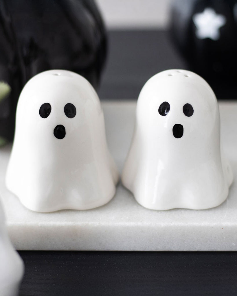 Lifestyle photo of the Rebel Romance ghost salt and pepper shakers on a marble tray, perfect for Halloween parties and gothic kitchen lovers.