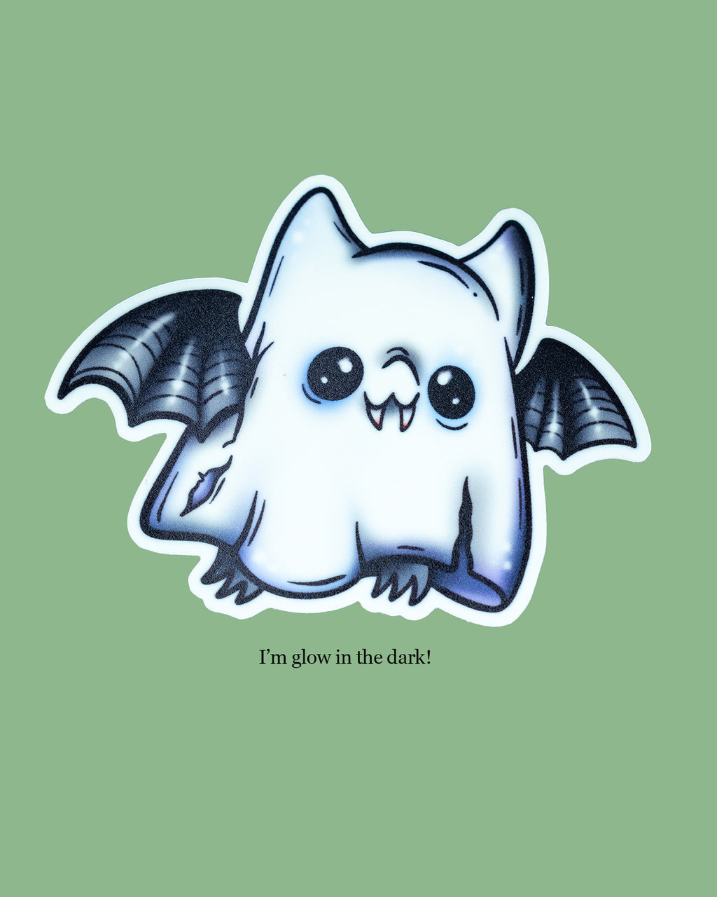 Glow in the dark ghost bat sticker featuring a cute cartoon bat dressed as a spooky ghost with torn edges and wide eyes. Black bat wings peek out from the ghost sheet design. Artwork by MilkTeef, perfect for Halloween lovers, spooky stationery collectors, and alternative style fans.
