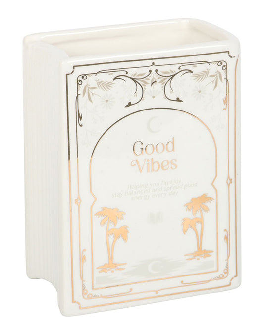 Angled view of Rebel Romance Good Vibes White Book Shaped Vase. This ceramic book-shaped vase in white with gold detailing adds charm to alternative home décor, making it perfect for book lovers and millennials seeking unique interior accessories.