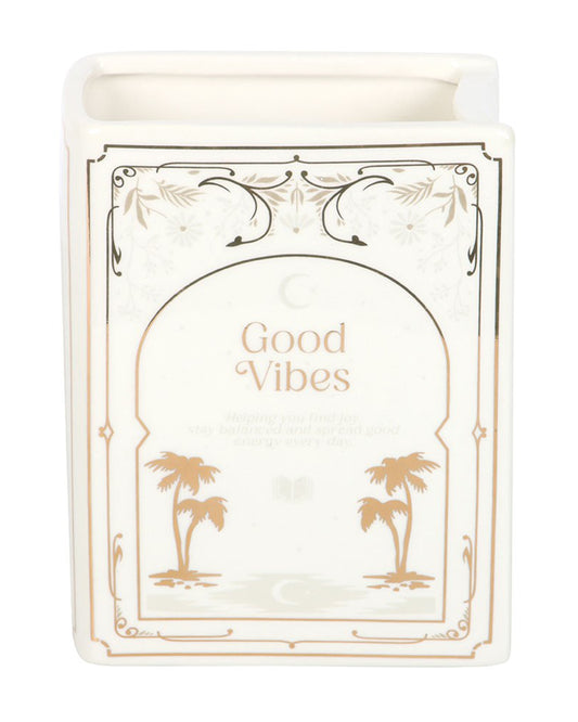 Close-up of Rebel Romance Good Vibes White Book Shaped Vase. This white ceramic vase with gold detailing and palm tree illustration is shaped like a standing book, bringing a literary flourish to home décor. Perfect for holding flowers or as a stylish statement piece.