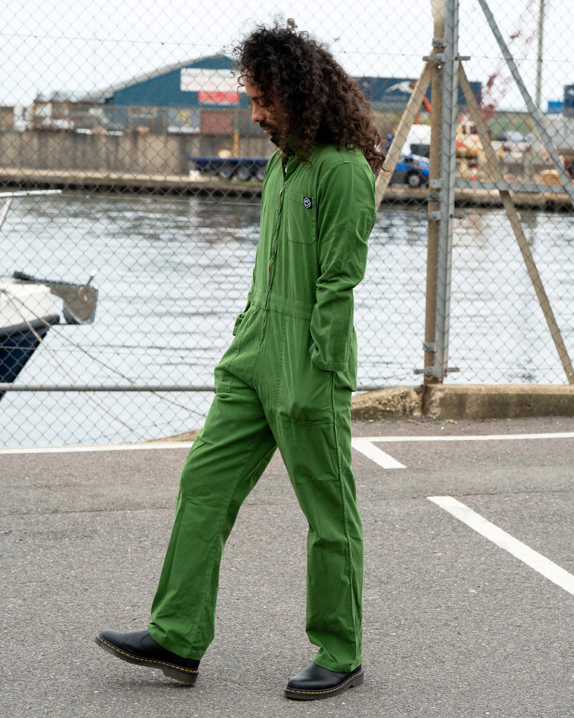 Richard wearing the Rebel Romance Forest Green Boiler Suit walking along a dockside with hands in pockets, showing relaxed everyday style.