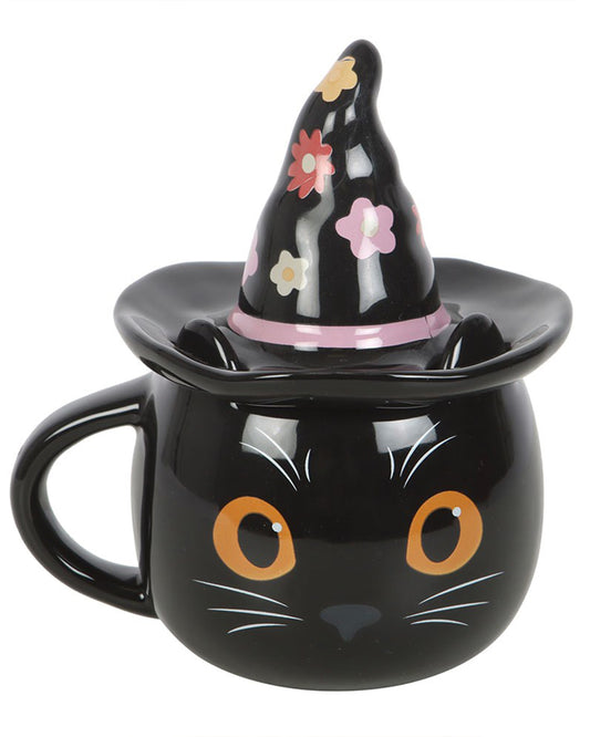Front-facing view of the Rebel Romance Groovy Witch Cat Mug. Features a black ceramic cat face with orange eyes and a floral witch hat lid with pastel flowers and a pink band. A quirky, seasonal mug for Halloween lovers and cat fans.