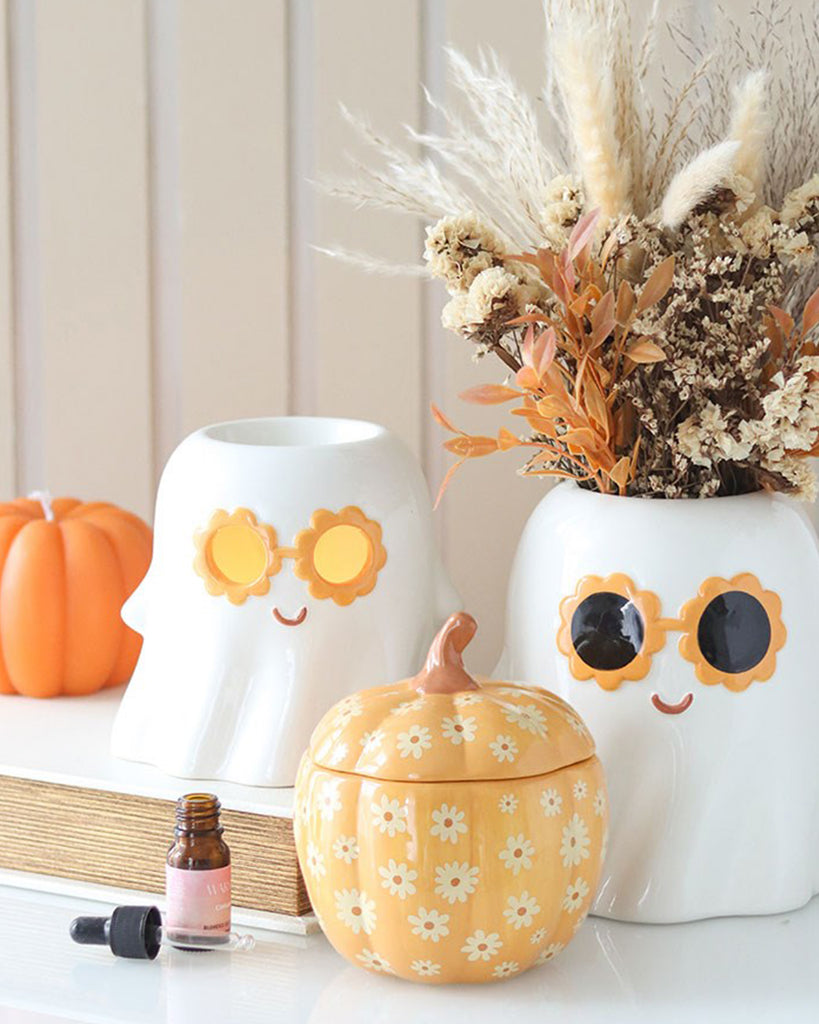 A Groovy Ghost oil burner with orange and black retro sunglasses, the matching vase sat beside is styled with autumn decor with a dried flower arrangement and orange ceramic pumpkin on a shelf. A cute, spooky and retro Halloween homeware piece from Rebel Romance.