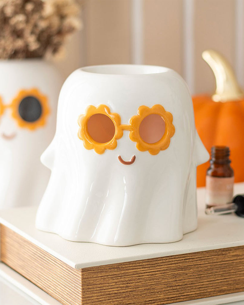 Groovy Ghost oil burner styled on a wooden shelf with a retro Halloween look, featuring orange sunglasses and an essential oil bottle beside it. A whimsical home scent accessory by Rebel Romance.