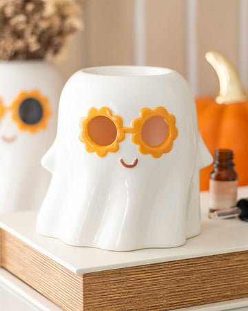Groovy Ghost oil burner styled on a wooden shelf with a retro Halloween look, featuring orange sunglasses and an essential oil bottle beside it. A whimsical home scent accessory by Rebel Romance.