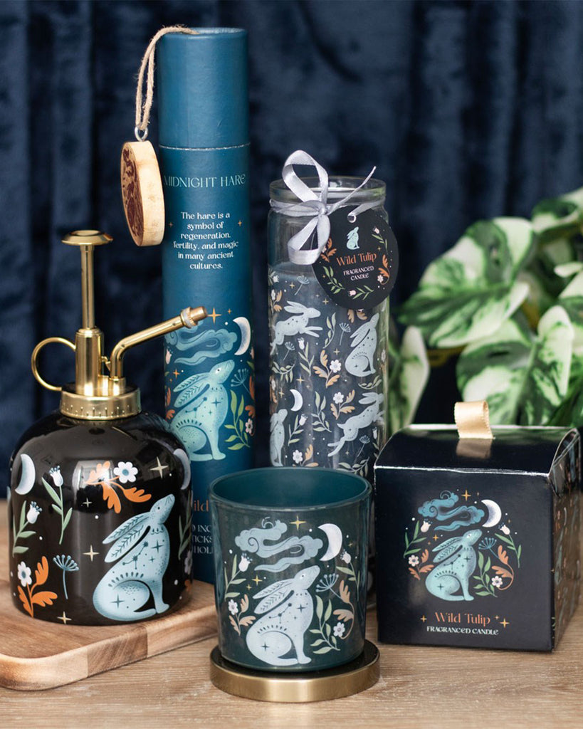 Midnight Hare Wild Tulip Tube Candle by Rebel Romance, featuring a tall glass candle with a mystical hare design surrounded by florals, moons, and stars. The set includes a matching candle holder, spray bottle, and gift box. Ideal for alternative home decor lovers.