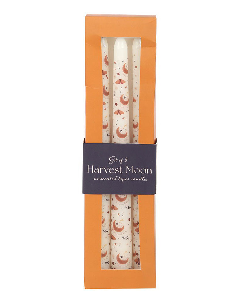 Box of three unscented taper candles decorated with copper moon, moth, and star motifs. The set is packaged in an orange and navy gift box with a window front.