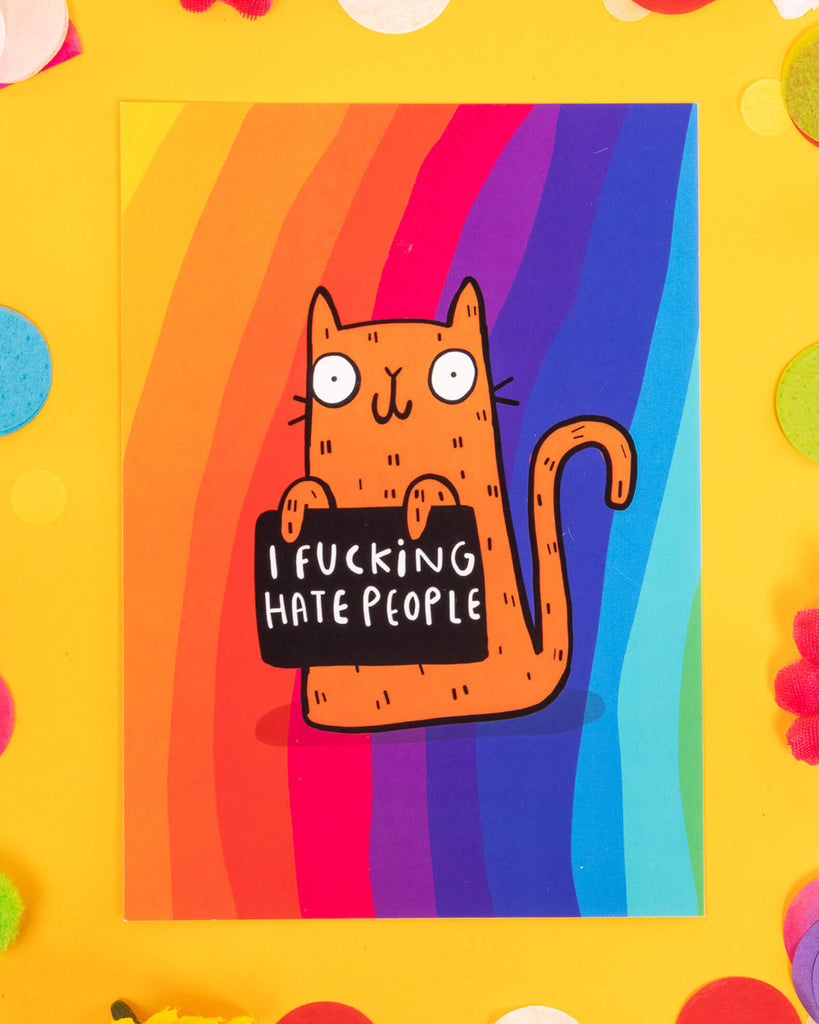 A bold A6 postcard featuring a cartoon orange cat holding a sign that says “I F*cking Hate People” on a vibrant rainbow background. Designed by Katie Abey, this sweary and honest card is ideal for millennials who love alternative humour, quirky stationery, and cards that tell it exactly like it is.