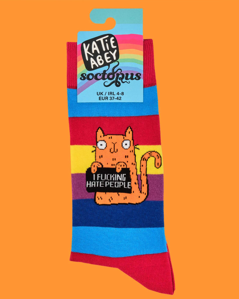 Product shot of one rainbow-striped sock with an orange cartoon cat holding a sign that says “I F*cking Hate People.” Label reads “Katie Abey x Soctopus,” with sizing info. Bright, fun and cheeky design.