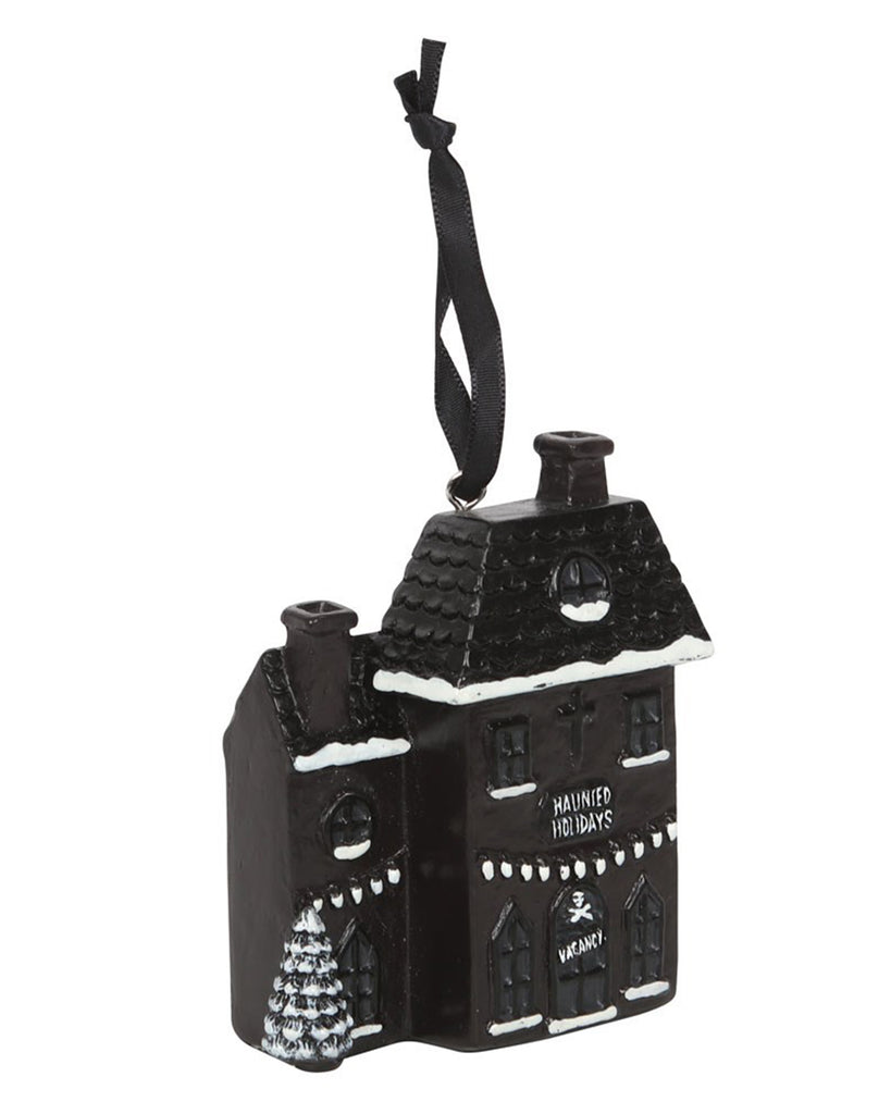 Angled view of the Haunted Holiday House Christmas ornament by Rebel Romance, featuring snow-topped rooftops, festive trees, and gothic windows with “Haunted Holidays” on the front and a skull-themed “VACANCY” sign above the door.