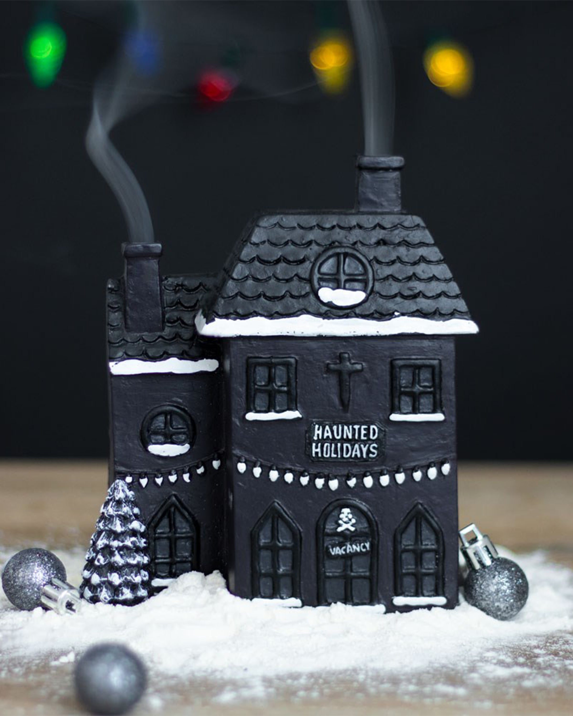 Close-up of the Haunted Holiday House Incense Burner by Rebel Romance, shaped like a spooky black Christmas house with snow accents and smoke drifting from twin chimneys.