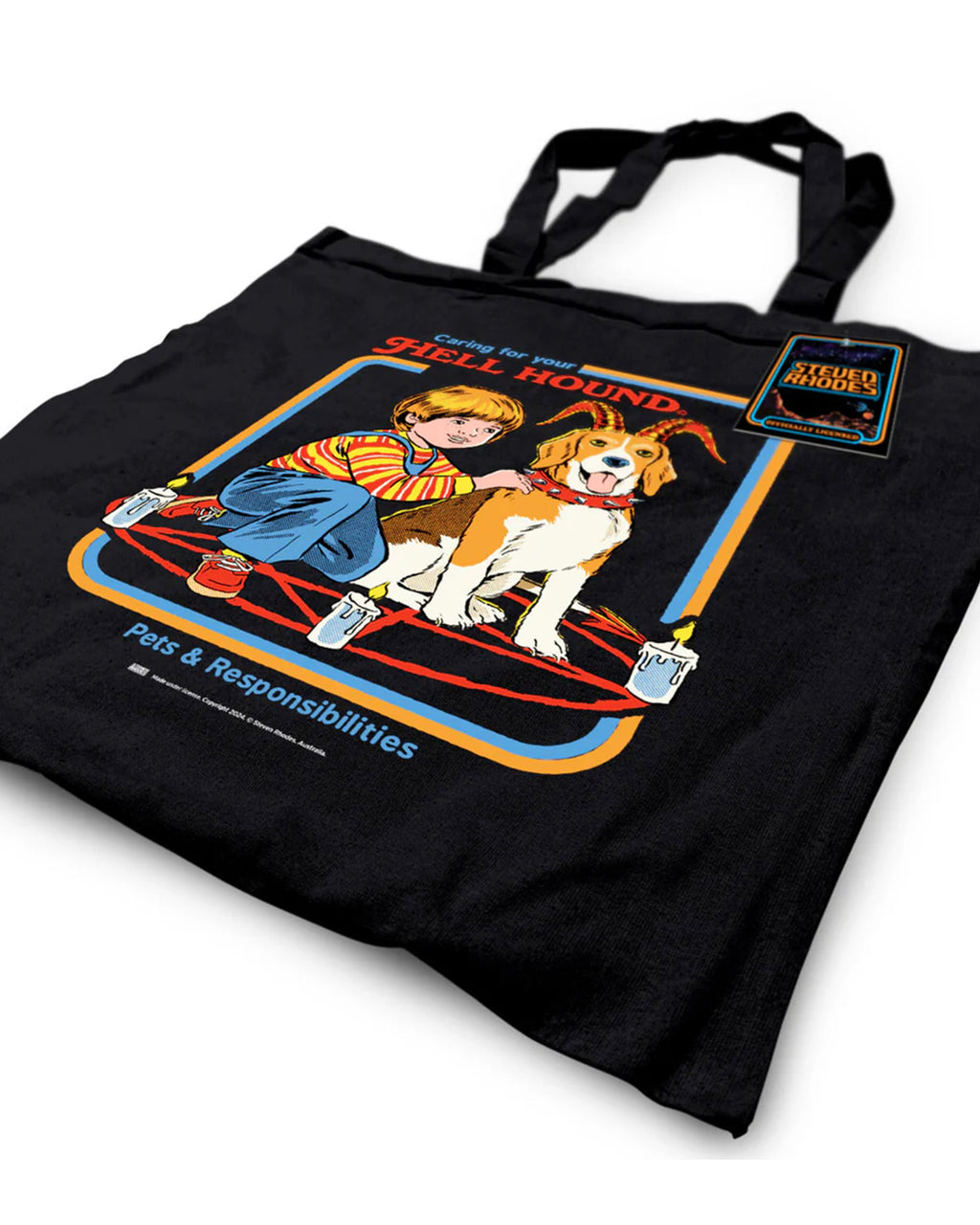 A black tote bag featuring Steven Rhodes’ “Caring for Your Hell Hound” design. The artwork showcases a boy kneeling next to a beagle with red horns, sitting in the middle of a summoning circle surrounded by lit candles. The text reads “Caring for Your Hell Hound” and “Pets & Responsibilities.”