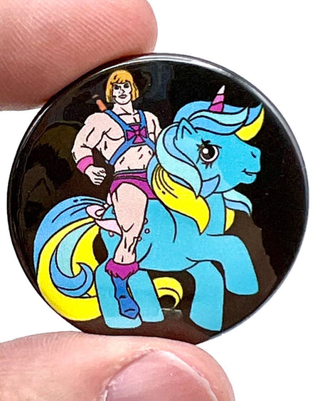 A round black 38mm button pin featuring a muscular cartoon man in pink and blue attire riding a cute blue unicorn with a yellow mane and pink horn. A nostalgic and humorous 1980s mashup accessory.