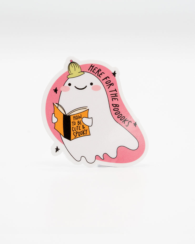 Cute die-cut vinyl sticker of a smiling ghost wearing a green beanie, holding a book titled “How to Be Cute & Spooky.” Surrounded by a pink border with the phrase “Here for the Booooks.” A fun bookish design perfect for Halloween lovers and cosy readers. Designed by Rebel Romance, a small UK brand celebrating alternative style, spooky vibes, and quirky millennial-friendly gifts.