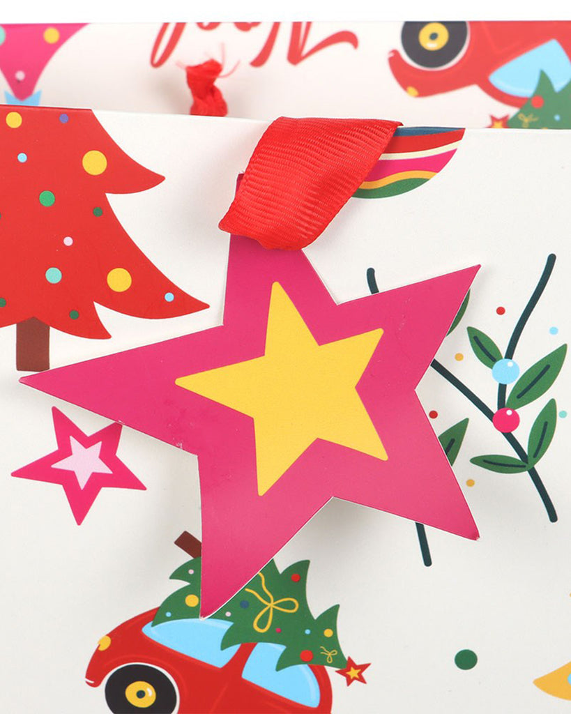 Close‑up of a Rebel Romance Nostalgic Christmas Print Gift Bag, showing a pink and yellow star tag and bold red ribbon handle. The festive print includes baubles, Christmas trees, and retro holiday motifs, giving gifts a fun, vibrant finish.