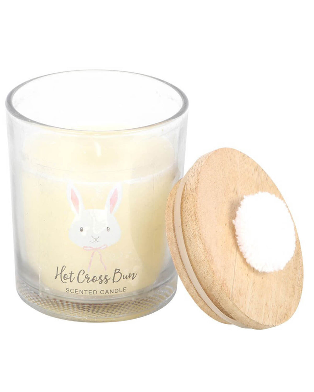 A clear glass candle jar with a soft yellow wax, featuring a cute bunny face design on the front and topped with a wooden lid adorned with a fluffy white pom-pom. The label reads “Hot Cross Bun Scented Candle.”