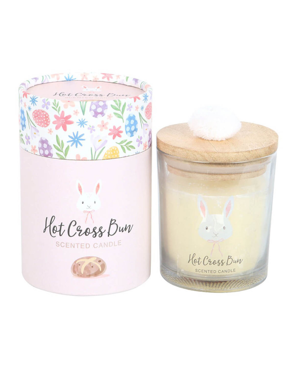 The candle displayed next to its pastel pink cylindrical gift box, which is decorated with colourful spring flowers, patterned Easter eggs, and a bunny illustration. The box is labelled “Hot Cross Bun Scented Candle.”