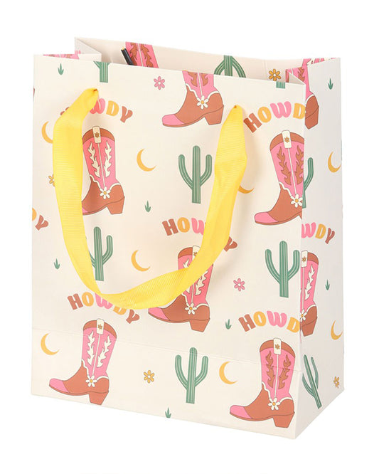 Medium Rebel Romance gift bag with a pink cowboy boot print, yellow ribbon handles and “Howdy” text, featuring cacti, moons and flowers in a playful Western design.