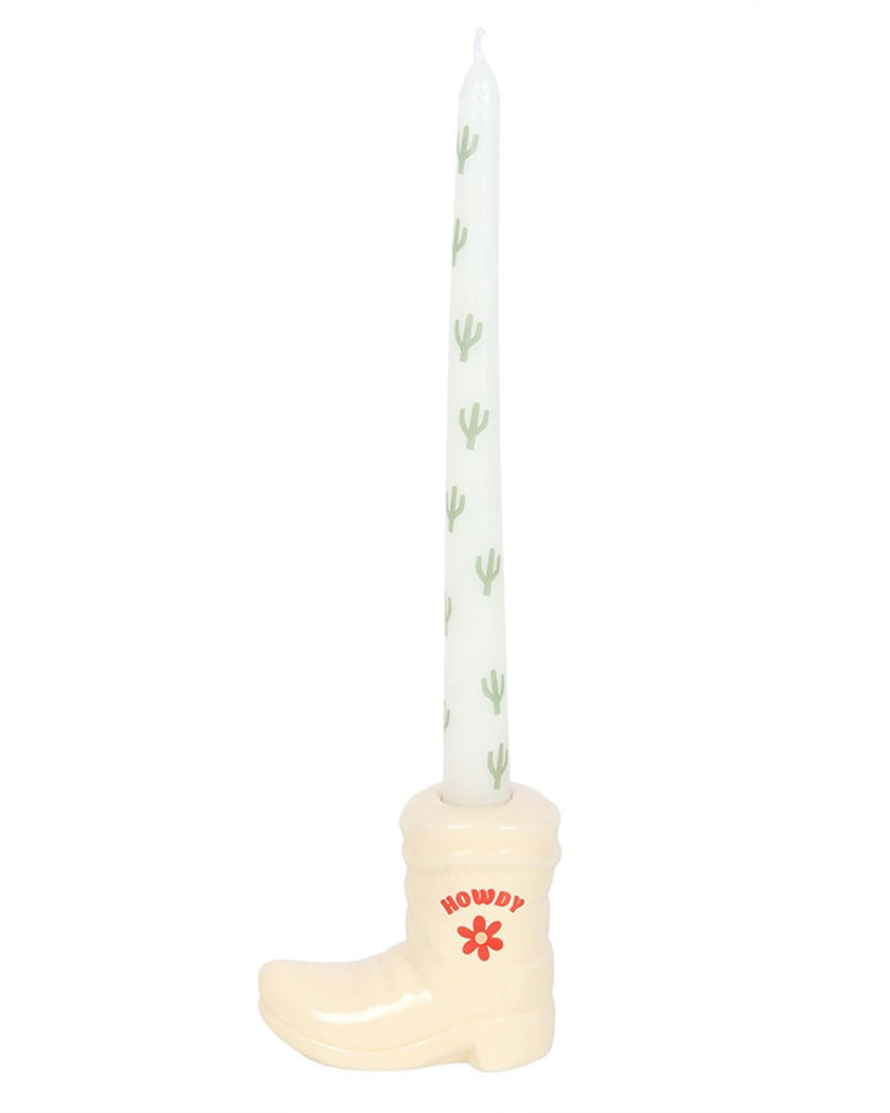Full view of the Rebel Romance cowboy boot candle holder with its matching cactus-print taper candle. The off-white boot has a fun Western aesthetic with "Howdy" and a red flower on the side, perfect for adding quirky charm to any space.