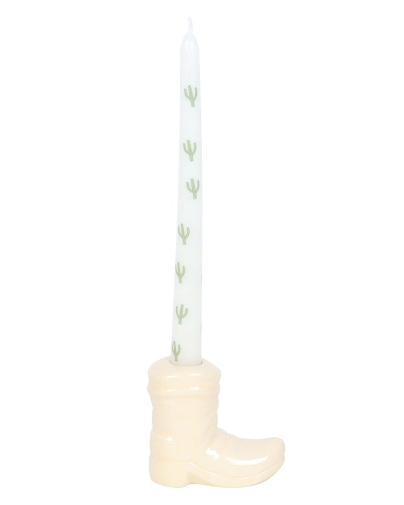 A white ceramic cowboy boot candle holder with a glossy finish, holding a tall white taper candle decorated with green cactus illustrations. The candle stands upright, showcasing its playful Western theme. Product by Rebel Romance, a small UK business celebrating alternative aesthetics.