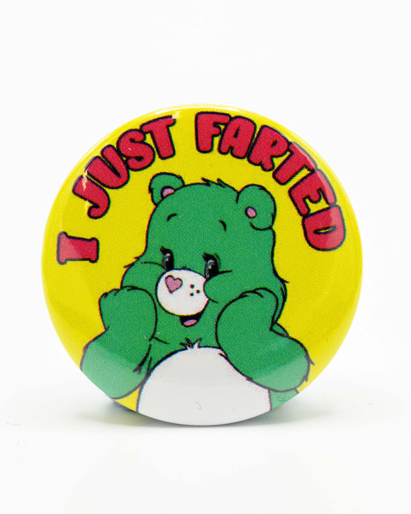 Round button pin badge featuring a retro-style green cartoon bear with a heart on its nose, covering its face in embarrassment. Surrounded by bold pink and red text that reads “I JUST FARTED” on a bright yellow background. A playful, cheeky design by Bite Your Granny, sold by Rebel Romance – a UK brand celebrating alternative and nostalgic humour with unique gifts and accessories.