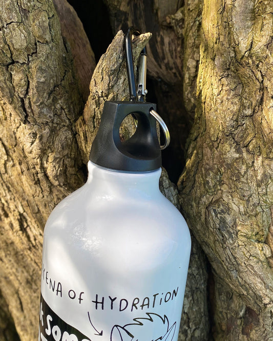 White aluminium water bottle featuring "The Hyena of Hydration" cartoon and slogan “Drink Some Water You Slag,” hanging from a carabiner on a tree trunk. Sold by Rebel Romance, a UK small business that celebrates alternative and humorous gifts and homeware.