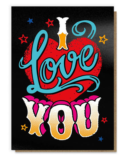  greeting card inspired by vintage tattoo designs featuring a bold red heart, vibrant blue script reading “I Love You,” and colourful retro typography with stars against a black background. The design is enhanced with black hot foil for a textured and striking finish, paired with a recycled kraft envelope.
