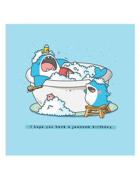 Flatlay of the Have a Jawsome Birthday card by Toastedink on a blue background. Includes a cartoon shark in a tub with bubbles and another shark beside it. A humorous, high-quality card for ocean fans, sold by Rebel Romance.