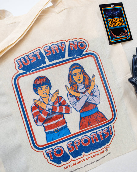 A natural cotton tote bag featuring a retro-style Steven Rhodes design with two children crossing their arms in an “X” shape and the text “Just Say No To Sports!” in bold, vintage-style lettering. The bag has a minimalist design with sturdy handles, perfect for daily use.